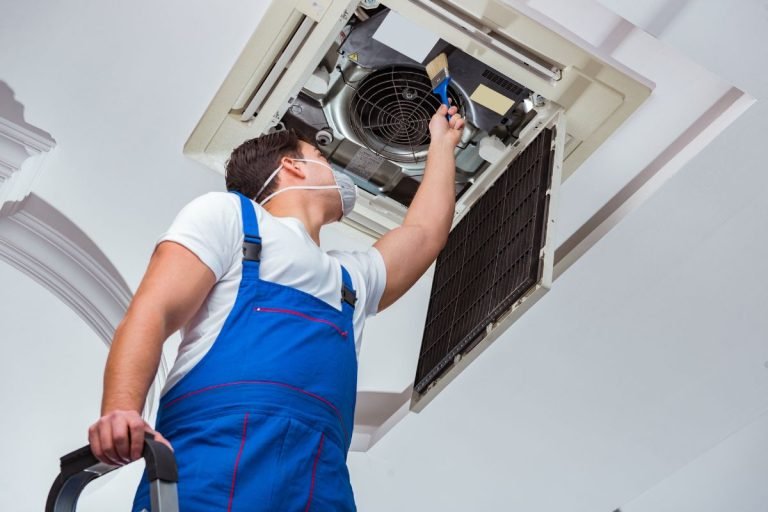 A man in blue overalls repairs an air conditioner, addressing mold issues in the HVAC unit.