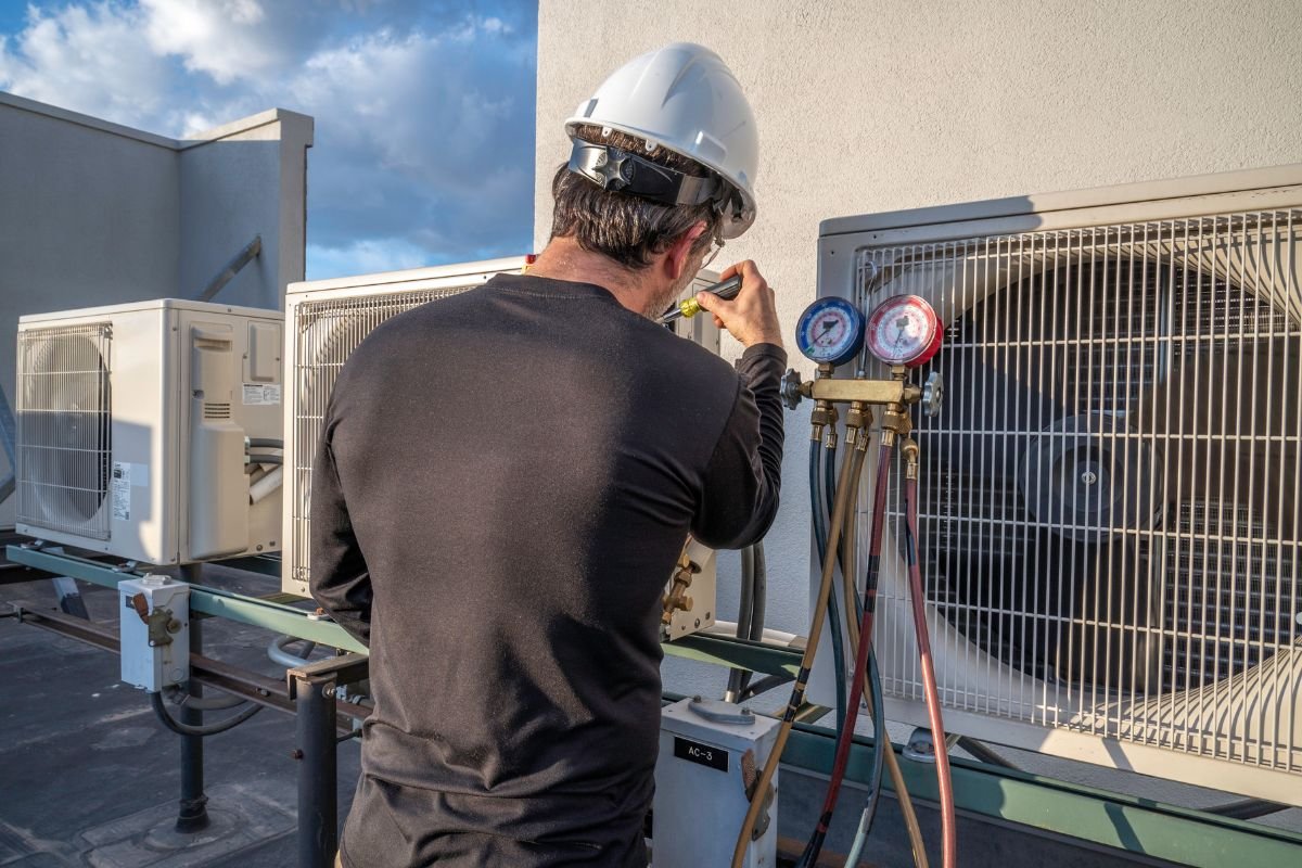 A man in a hard hat inspects air conditioning units as part of a mold removal service.